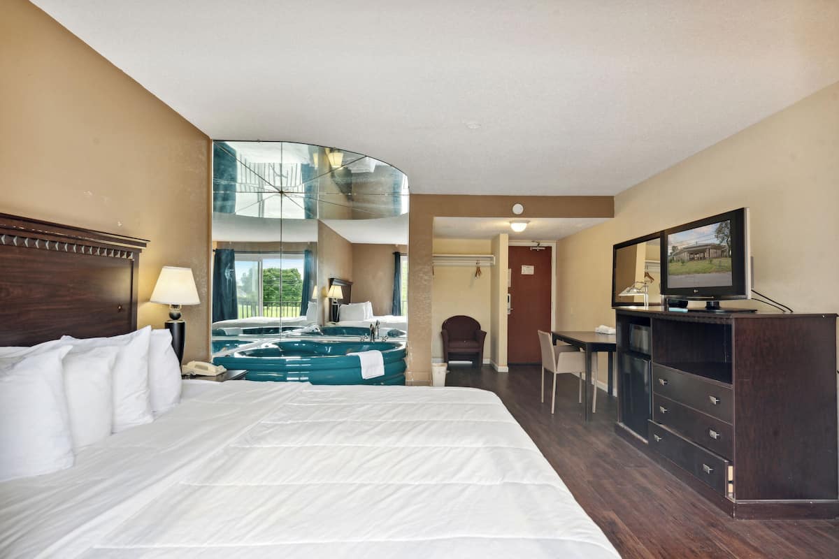 Habitación de hotel con una cama grande, televisión, escritorio, silla, lámpara de escritorio, teléfono y bañera de hidromasaje.