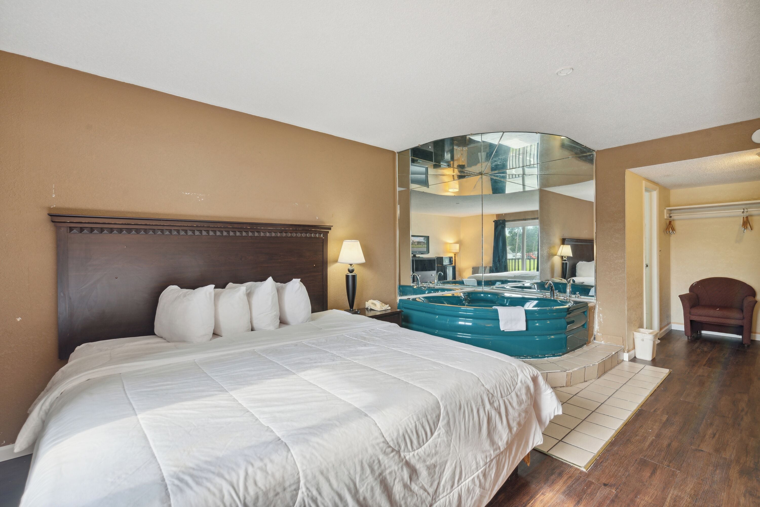 A hotel room with a large bed, a sitting area with a chair, a large mirror, and a bathtub.