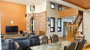 Una sala de estar moderna con una mesa de comedor de vidrio, sillones de cuero, una pared decorativa de ladrillo, una chimenea y una escalera de madera.