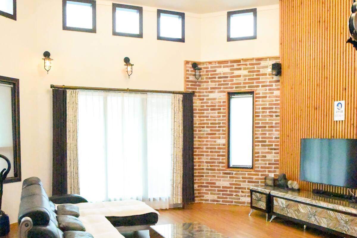 Un salon spacieux avec un long canapé, une table basse et un téléviseur fixé à un mur en bois.