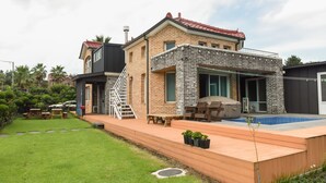 Una casa de dos pisos con fachada de ladrillo, techo de tejas rojas, un porche cubierto y una piscina.