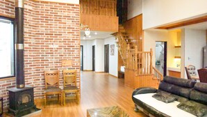 Un salón amplio con pared de ladrillo, suelo de madera, un sofá, una chimenea y una escalera que lleva a un nivel superior.