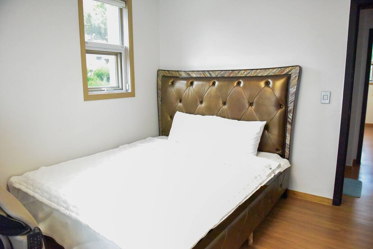 Un lit simple avec une tête de lit capitonnée, une fenêtre au-dessus et un plancher en bois.
