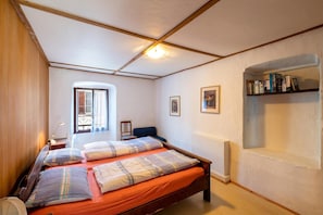 A bedroom with a bed, a window, a bookshelf, and a door. - Casa Merlot in Caslano for 4 (Caslano)