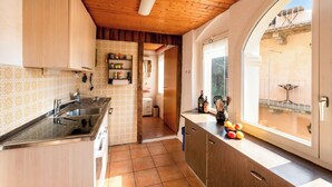 A kitchen with a large sink, wooden cabinets, a tiled backsplash, and a window with a view of the outside. - Casa Merlot in Caslano for 4 (Caslano)