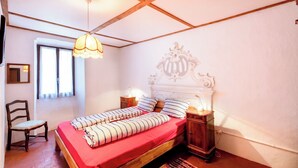 A bedroom with a wooden bed, a chair, a bedside table with a lamp, and a decorative headboard. - Casa Merlot in Caslano for 4 (Caslano)