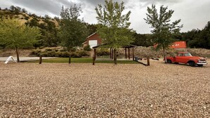A gravel parking area with a red vintage car, a gazebo, and a building with a red roof in the background.