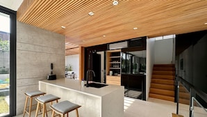 A modern kitchen with a central island, bar stools, and a wooden ceiling.