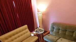 A living room with a beige sofa, a green sofa, and a small round table with a vase. - Amazing 1934 deco house. (Wonthaggi,)