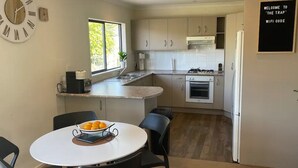 A compact kitchen with a round dining table, a clock on the wall, and a sign indicating a WiFi code. - Amazing 1934 deco house. (Wonthaggi,)