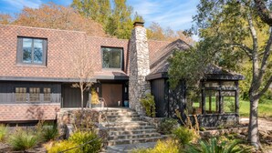 A modern house with a stone chimney, a wooden deck, and a stone staircase leading to the entrance.