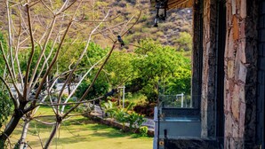 A building with a stone exterior and a view of a landscaped garden with a tree and a fence. - The Divine Hills Resort | Suites with Private Pool | Near IIM Udaipur (Udaipur)