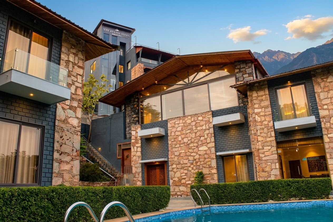 Un hotel moderno con arquitectura de piedra y vidrio, piscina y vistas a la montaña.