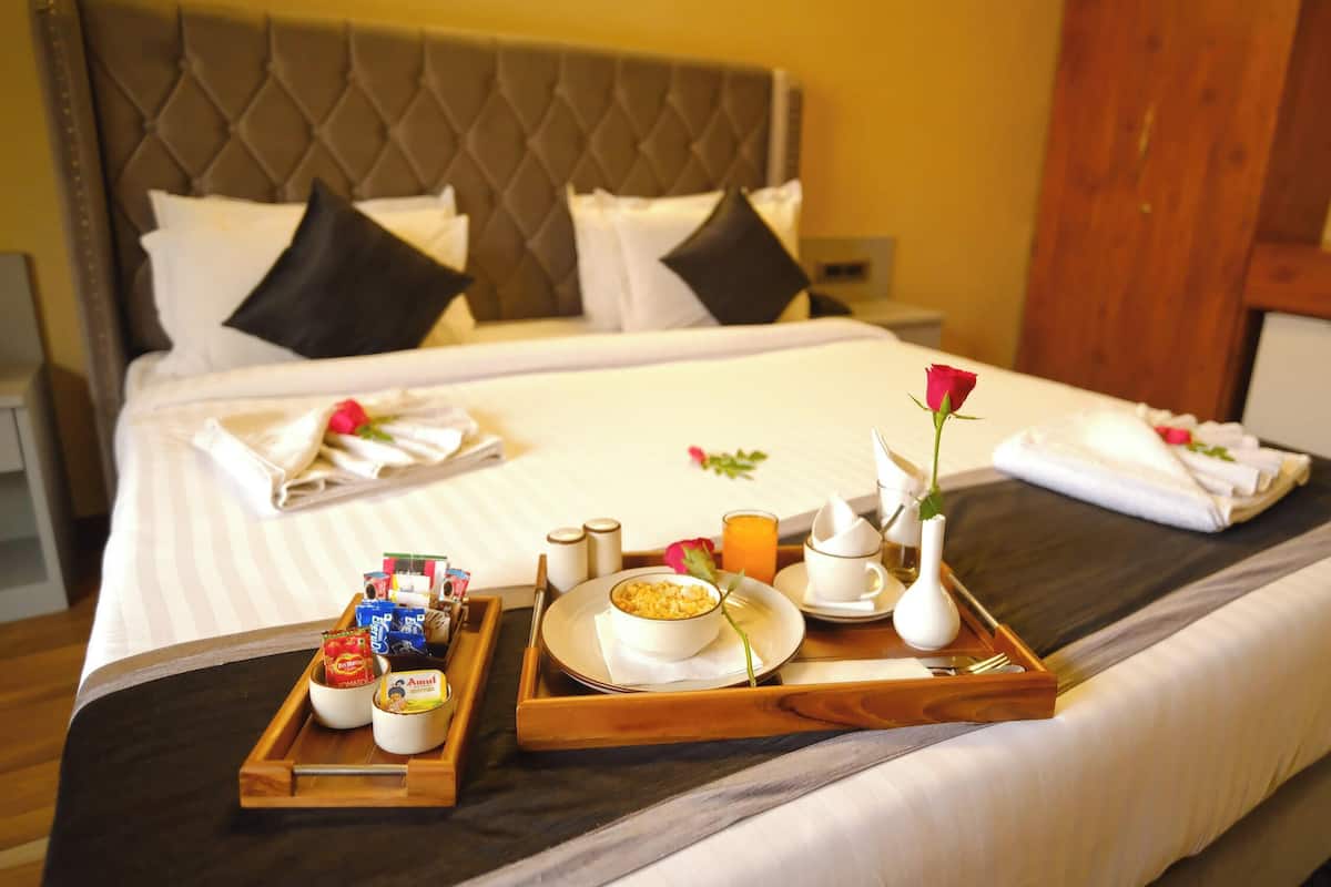 A neatly made bed with pillows, a tray with food items, and a rose on the bed.