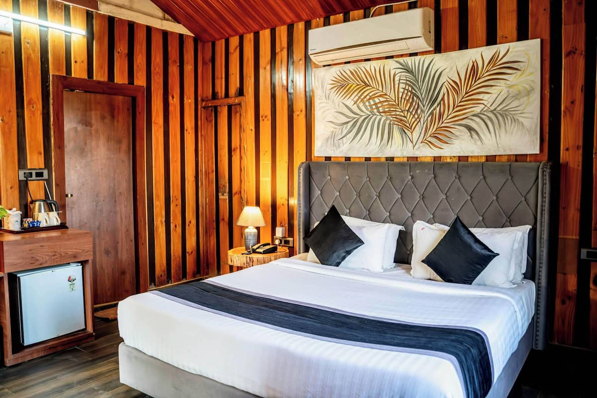 A wooden-paneled room with a bed, a nightstand, a lamp, and a small refrigerator.