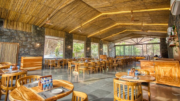 A spacious indoor dining area with bamboo ceilings, stone walls, and large windows offering views of the outdoors. - The Divine Hills Resort | Suites with Private Pool | Near IIM Udaipur (Udaipur)