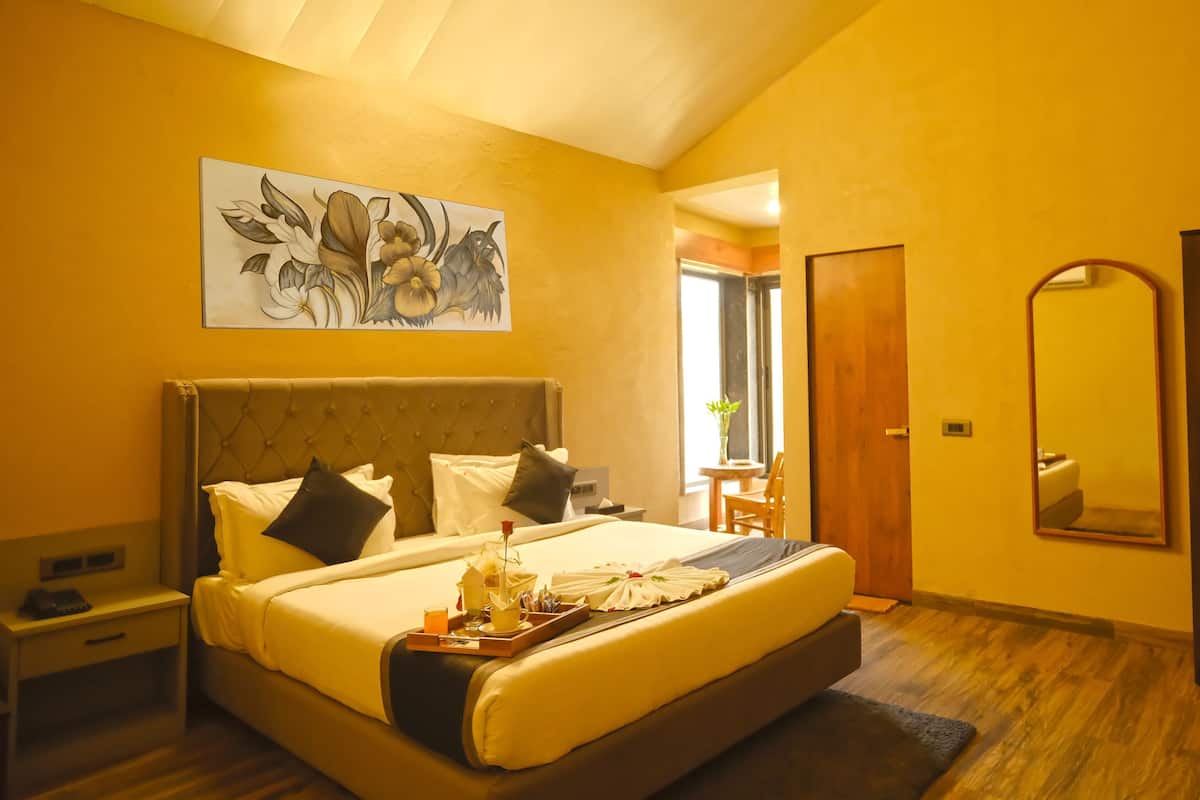 A hotel room with a large bed, bedside table, a mirror, and a painting on the wall.