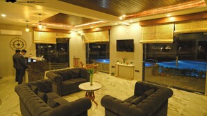 A well-lit lobby with dark leather sofas, a marble floor, and large windows overlooking a pool. - The Divine Hills Resort | Suites with Private Pool | Near IIM Udaipur (Udaipur)
