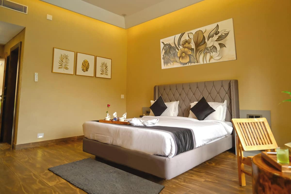 A hotel room with a bed, a bedside table with a tray, a chair, and artwork on the walls.