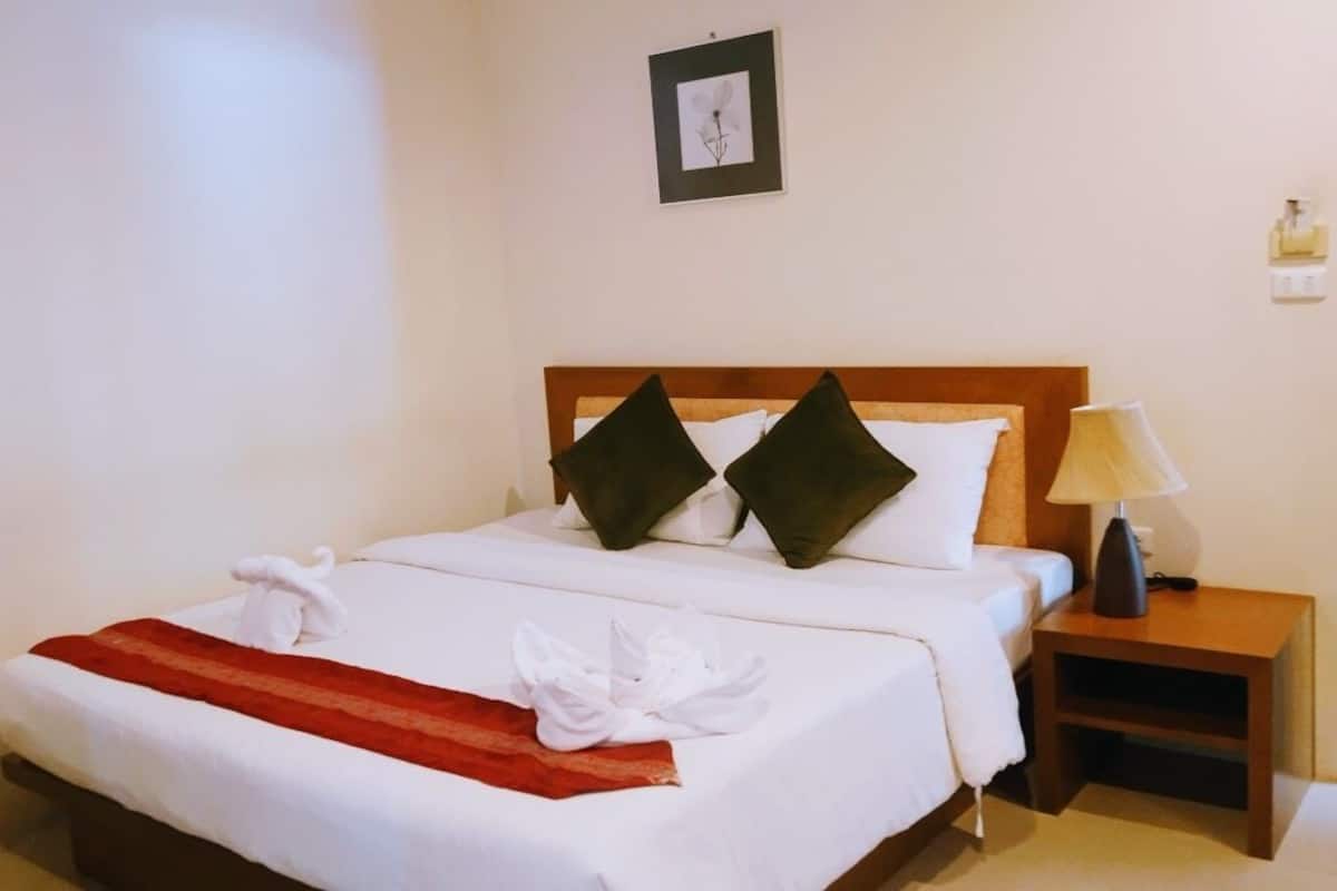 Ein ordentlich bezogenes Bett mit weißen Leinen und einer rot gestreiften Decke, zwei Kissen, eine Nachttischlampe und ein gerahmtes Bild an der Wand.