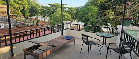 A balcony with a wicker lounge chair, two chairs, and a small table.