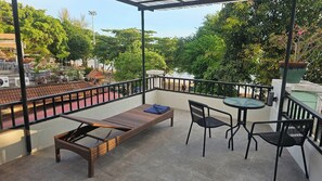 A balcony with a wicker lounge chair, two chairs, and a small table.