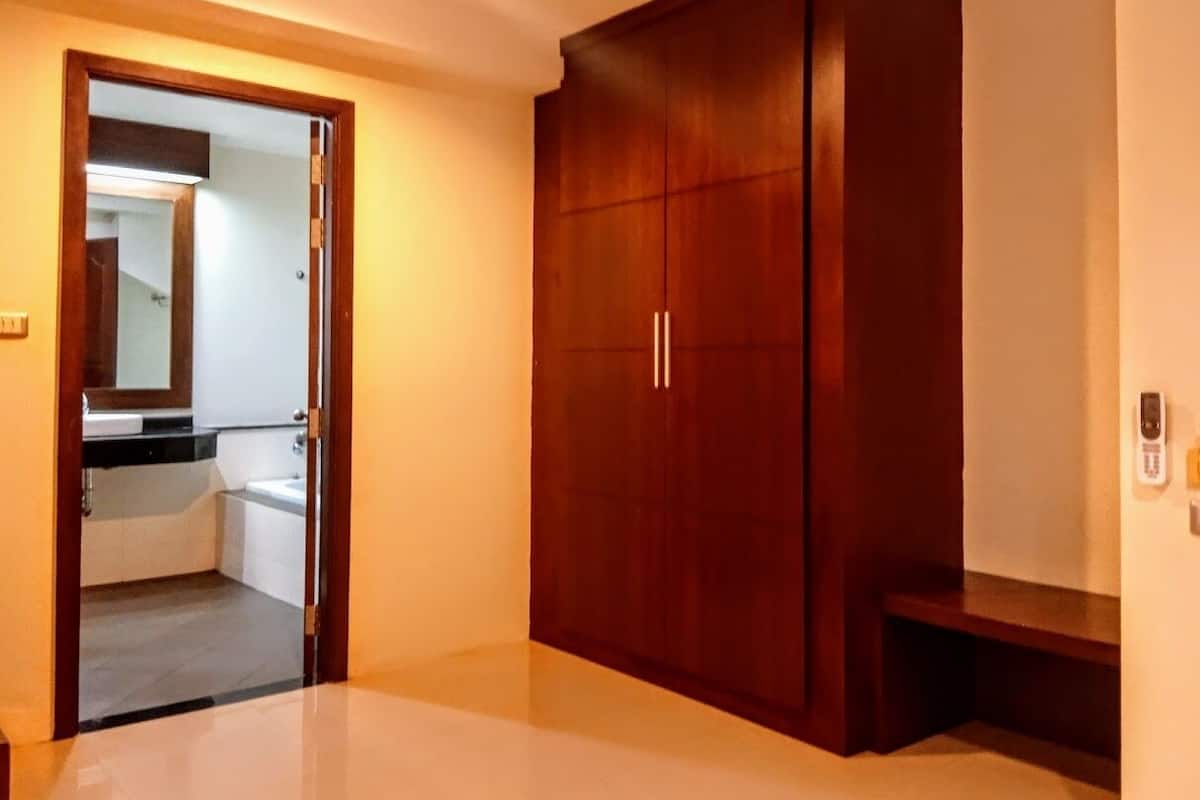Ein Zimmer mit Holzschrank, Spiegel und Blick ins Badezimmer mit Badewanne.