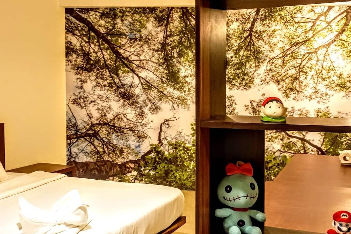 Ein Hotelzimmer mit Bett, einer Wand mit Baum-Fresko und einem Regal mit Kuscheltieren.