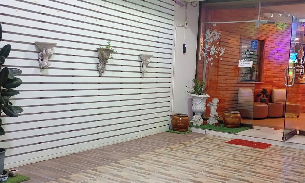 Un vestíbulo de hotel con una pared de listones blancos, plantas en macetas y un puerta de vidrio que da a una zona de estar.