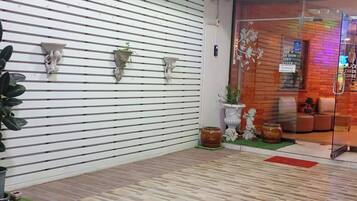 Un vestíbulo de hotel con una pared de listones blancos, plantas en macetas y un puerta de vidrio que da a una zona de estar.