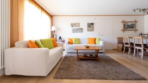A living room with a white sofa, a wooden coffee table, and a dining area with wooden chairs.