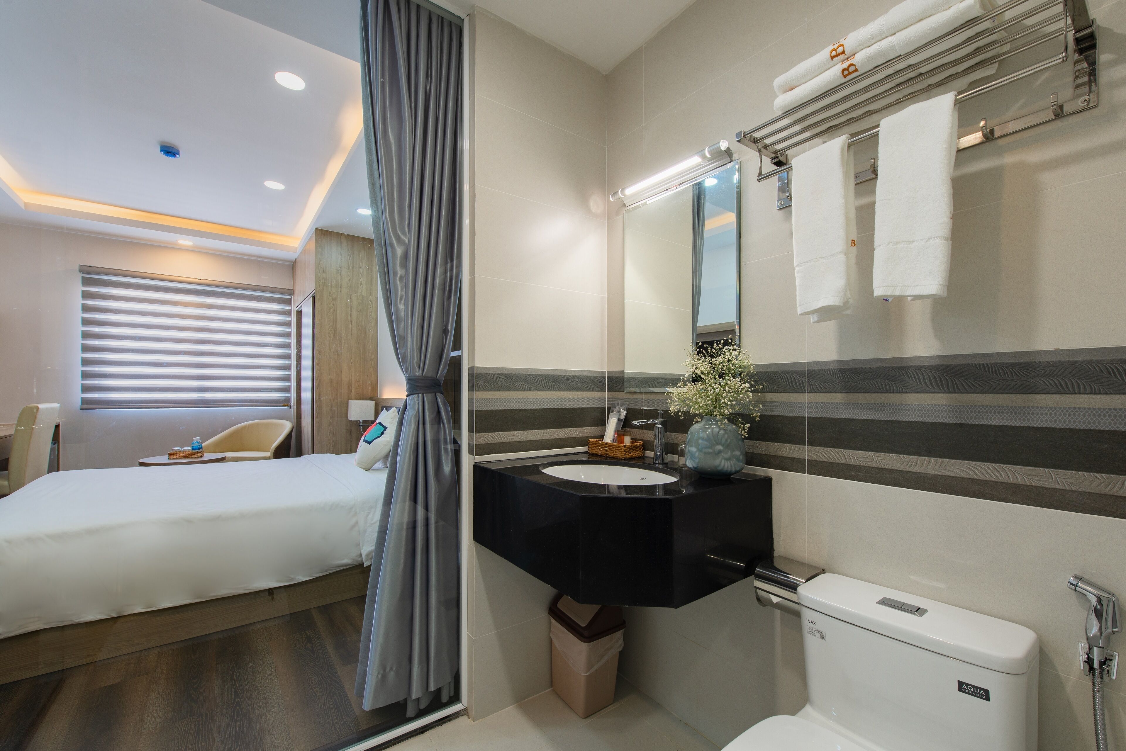 A modern hotel bathroom with a large mirror, a black sink, and a toilet.