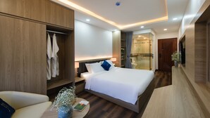 Ein modernes Hotelzimmer mit einem großen Bett, Nachttischen, einem Kleiderschrank, einer gläsernen Dusche und einer Sitzecke mit einem Sessel und einem kleinen Tisch.