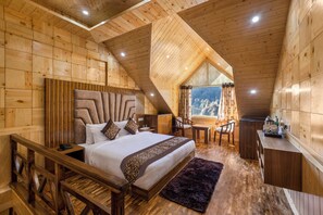 A wooden cabin bedroom with a large bed, a desk, and a view of the outdoors. - Sterling Shivalik Chail (Shimla)
