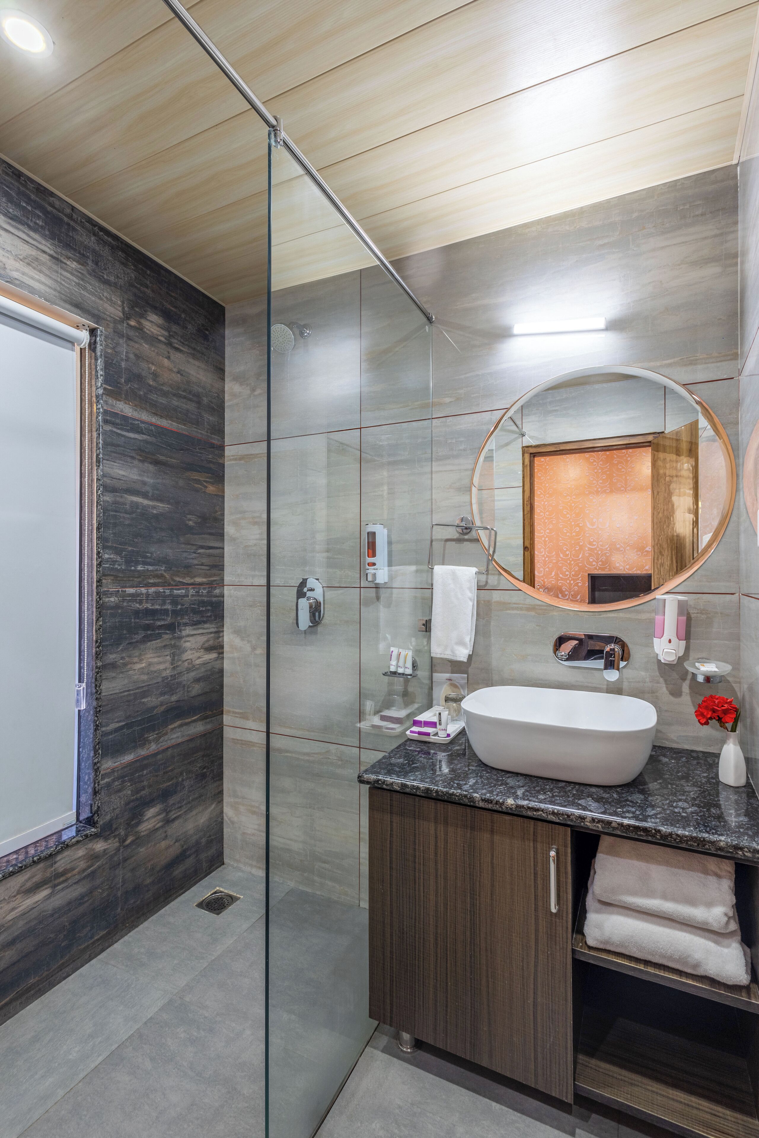 Une salle de bain moderne dotée d’une douche à parois de verre, d’une baignoire sur pieds et d’un meuble-lavabo en bois surmonté d’un plan de travail en marbre.