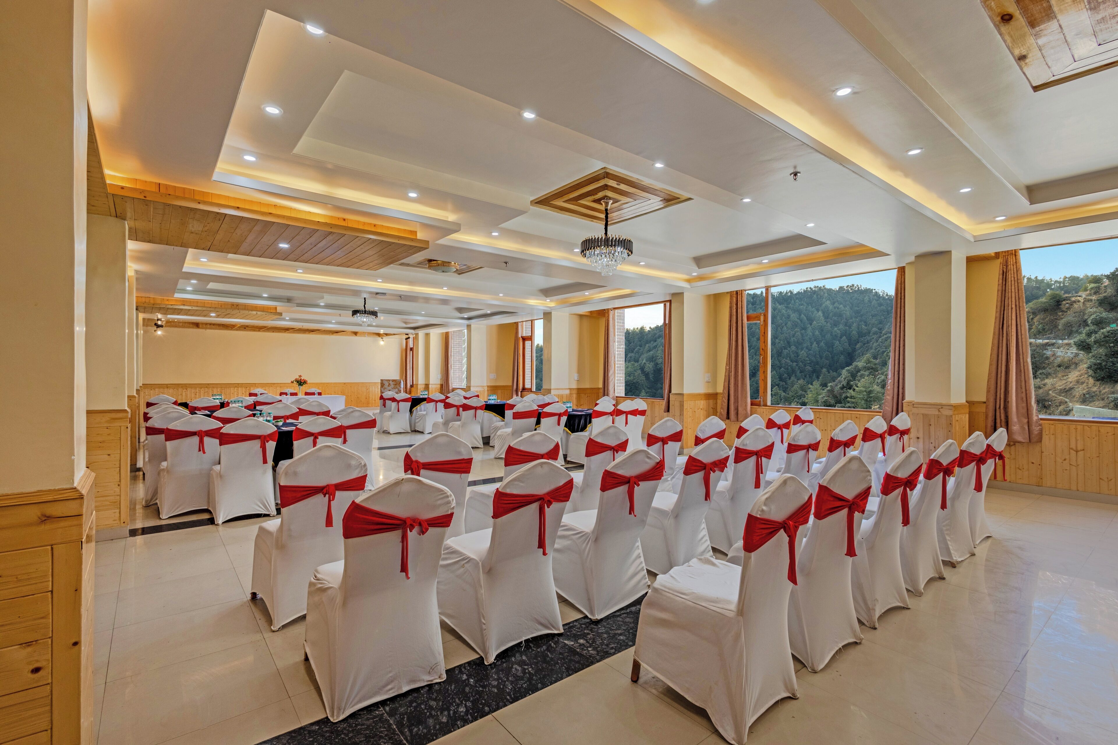 A conference room with rows of chairs, a wooden ceiling, and large windows with a view of a forested area.