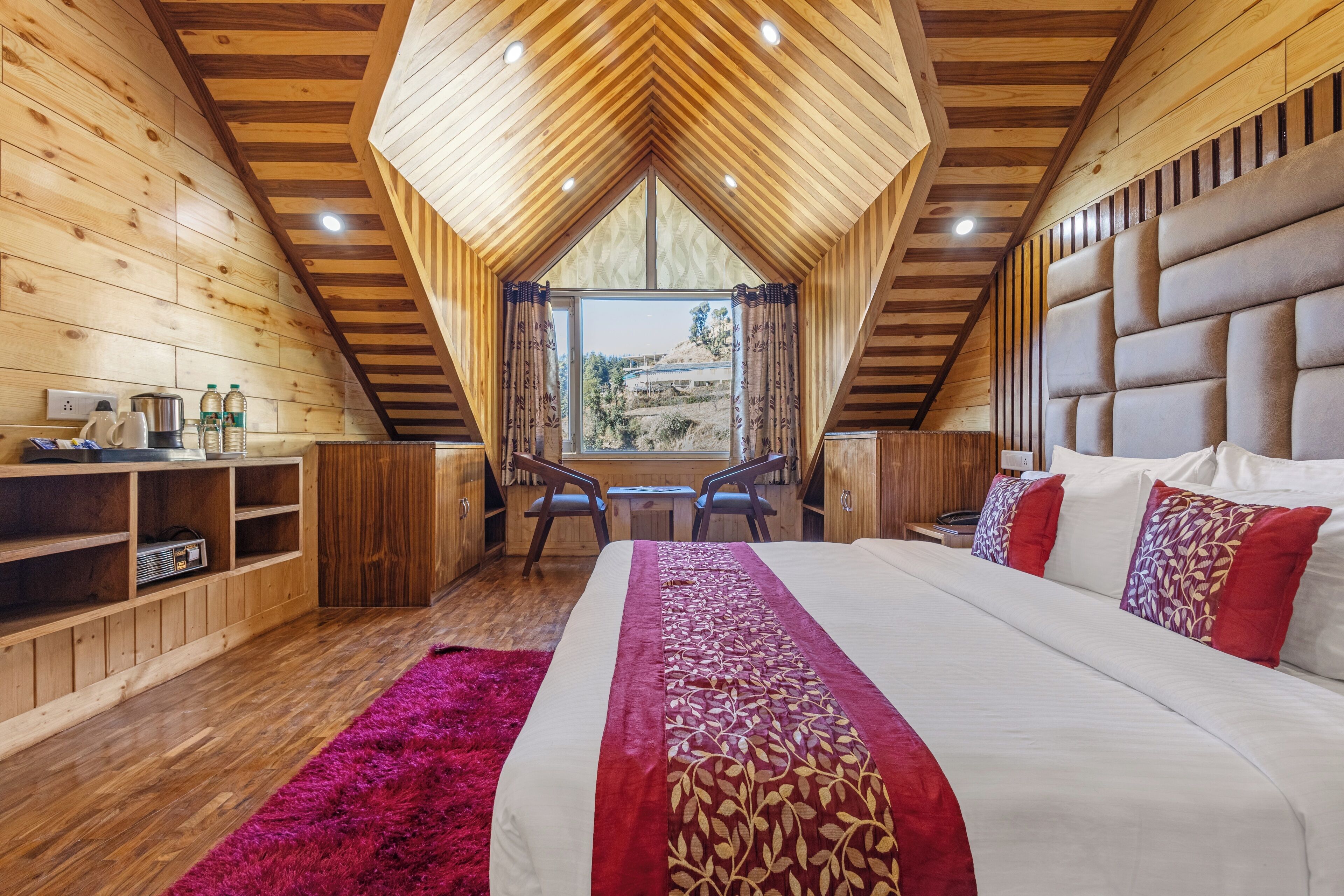 Ein Schlafzimmer mit einem großen Bett, Holzwänden, einer geneigten Decke, einem Fenster und einem Schreibtisch mit Stühlen.