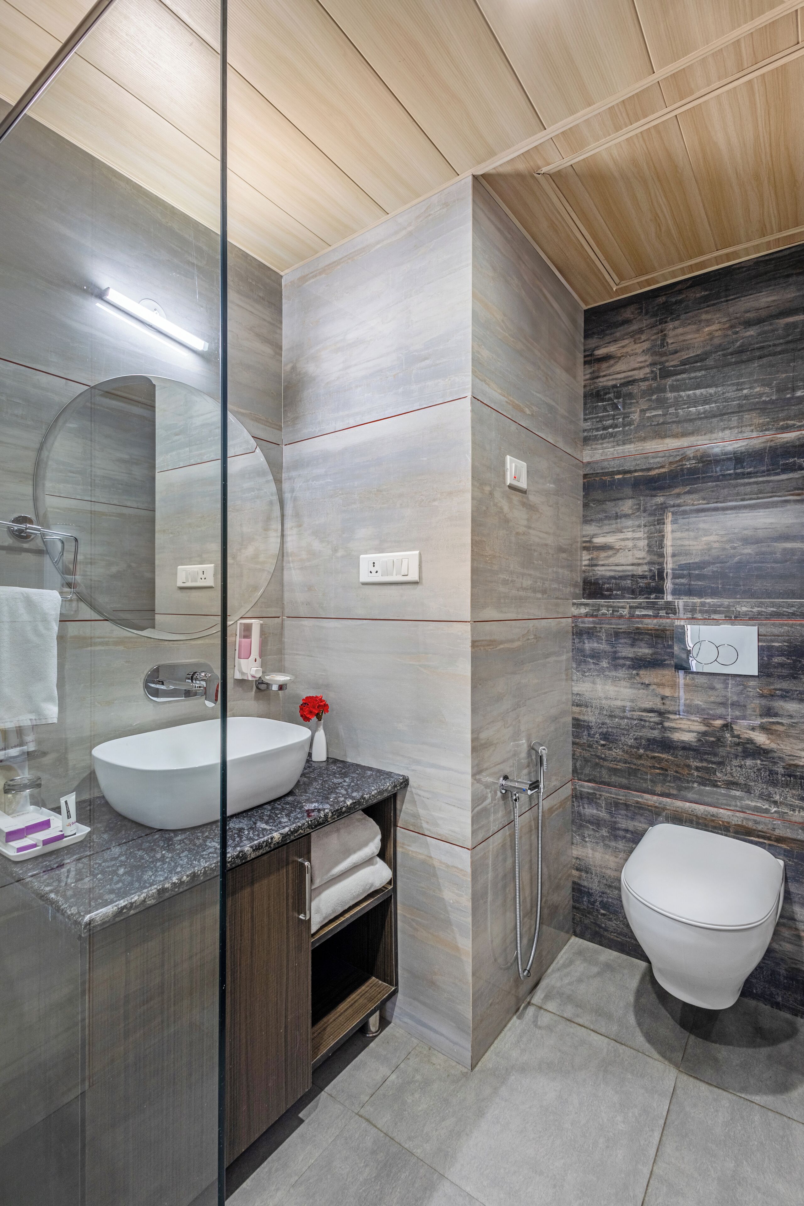 A modern bathroom with a glass-enclosed shower, a white sink, and a marble-tiled wall.