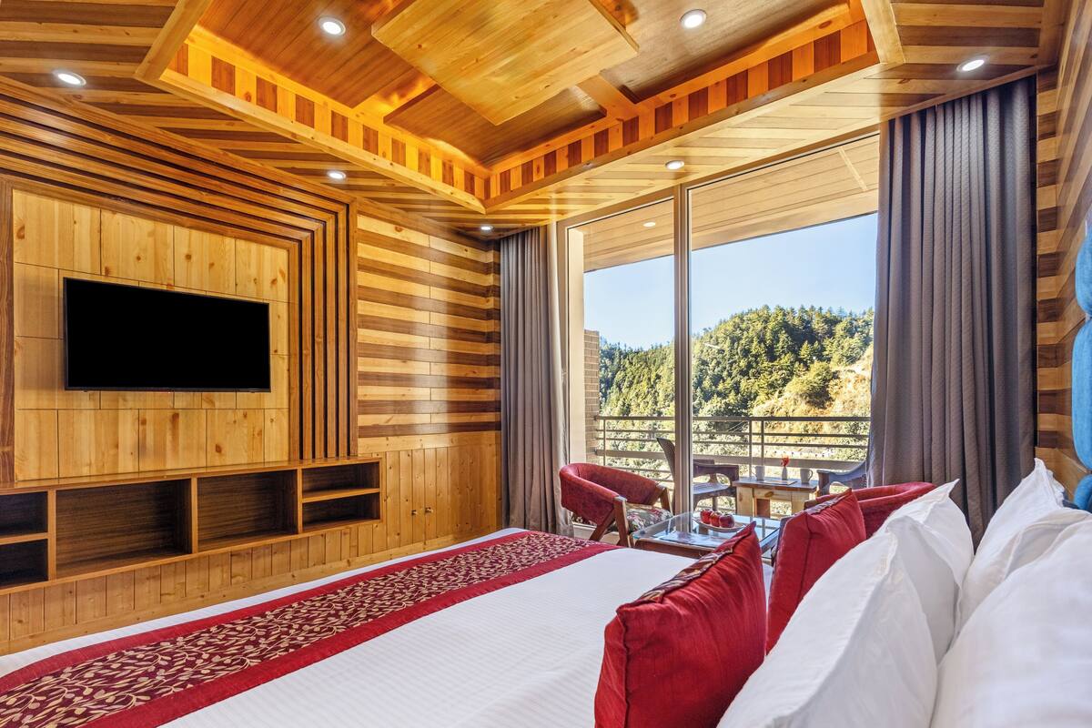 A wooden-paneled room with a large bed, a flat-screen TV, and a view of a forested area.