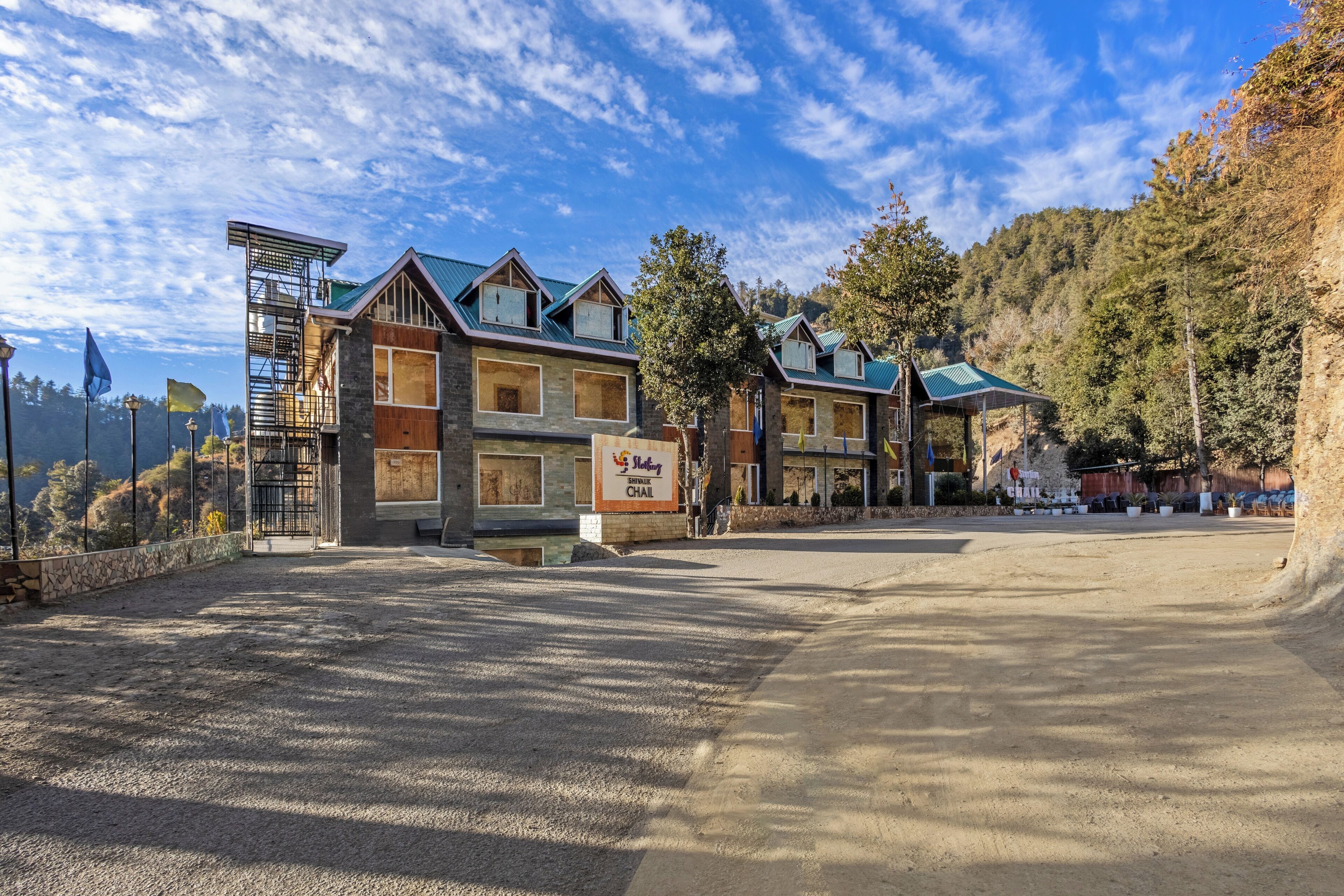 A multi-story hotel with a stone facade and green roofs, located in a mountainous area with a clear sky.