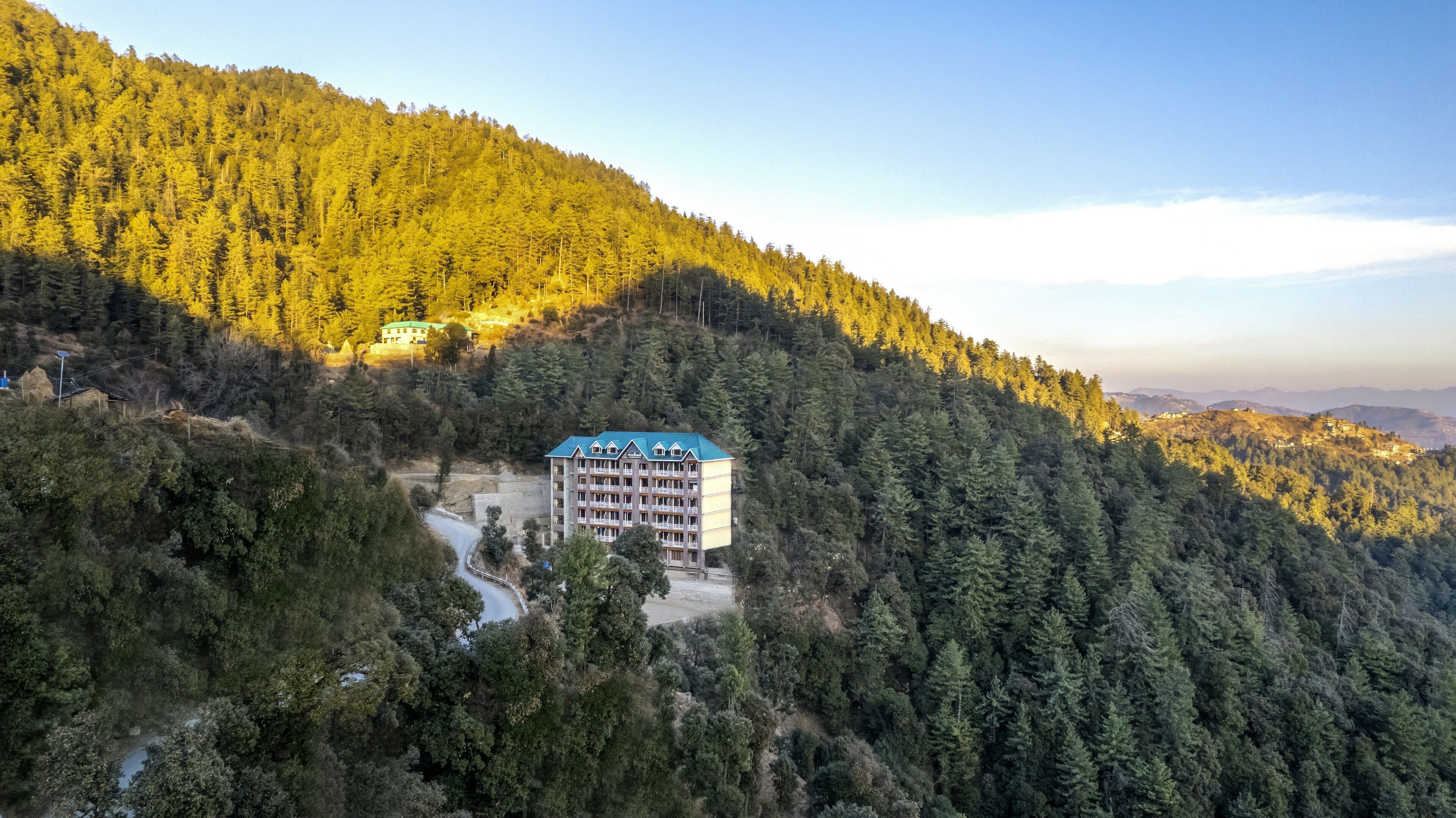 A multi-story hotel with a blue roof nestled in a forested valley.