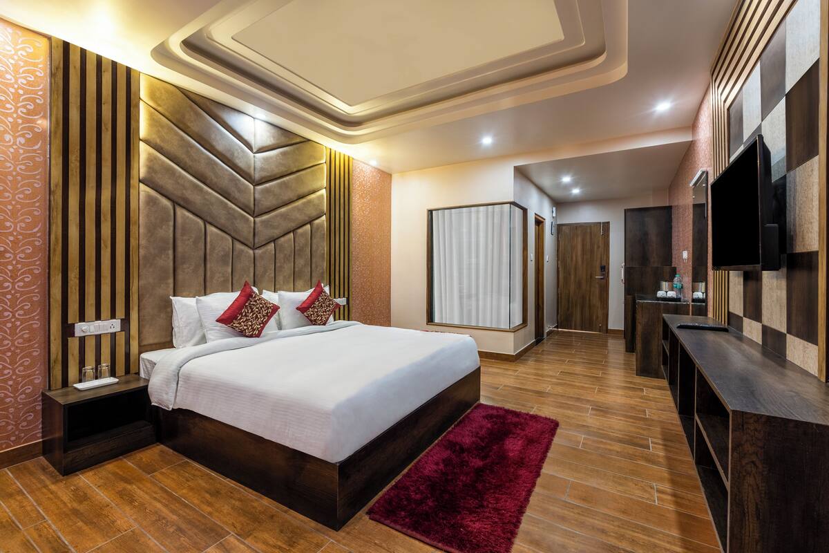 A modern hotel room with a large bed, wooden headboard, a TV, and a desk.