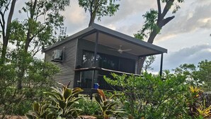 Una casa moderna de dos pisos con techo plano, rodeada de exuberante vegetación y árboles.