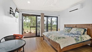 Un dormitorio con una cama de madera, una mesita pequeña y un ventanal amplio.
