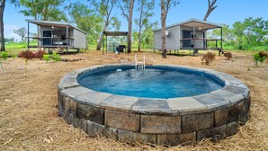 Una piscina circular rodeada de muros de piedra, con dos cabañas al fondo.