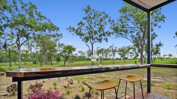 Un patio al aire libre con una terraza de madera, dos taburetes de bar y una mesa de vidrio.