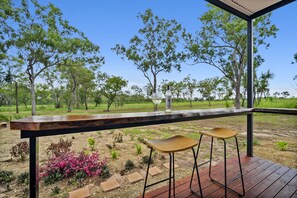 Un patio al aire libre con una terraza de madera, dos taburetes de bar y una mesa de vidrio.