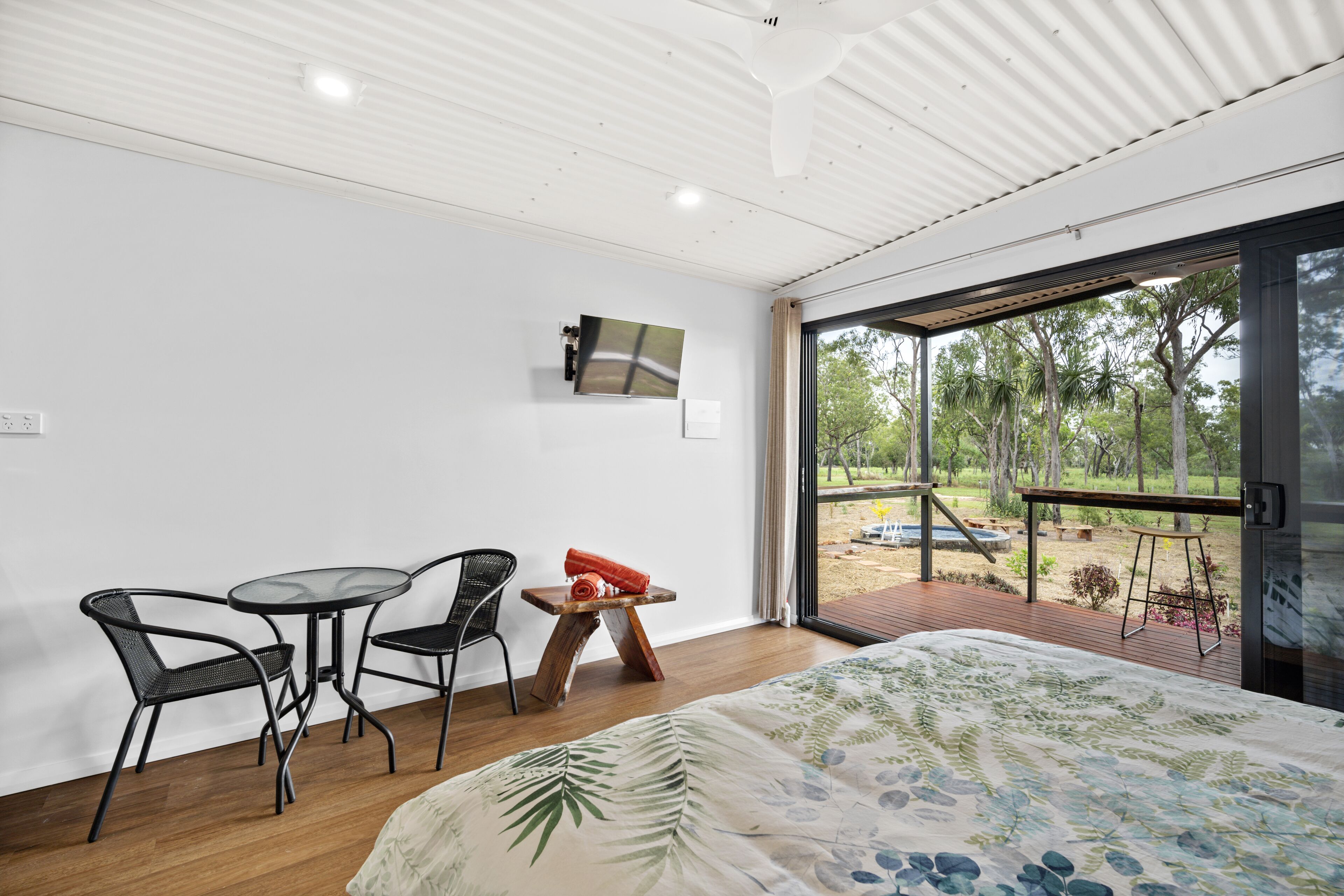 A modern room with a bed, a small table, two chairs, and a TV mounted on the wall.