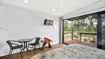 A modern room with a bed, a small table, two chairs, and a TV mounted on the wall.