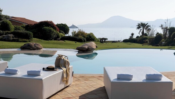 A poolside area with lounge chairs and towels, a view of the sea, and a mountainous landscape in the background. - Villa Padulella 8 2 Emma Villas (Portoferraio)